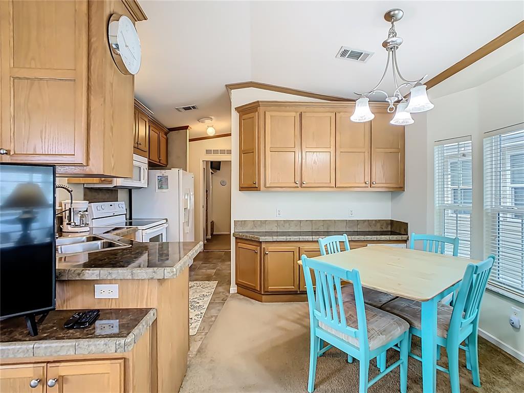 A kitchen and dining area with light wood cabinets, dark countertops, and blue chairs — 9000 US HWY 192 UNIT 324, CLERMONT, FL