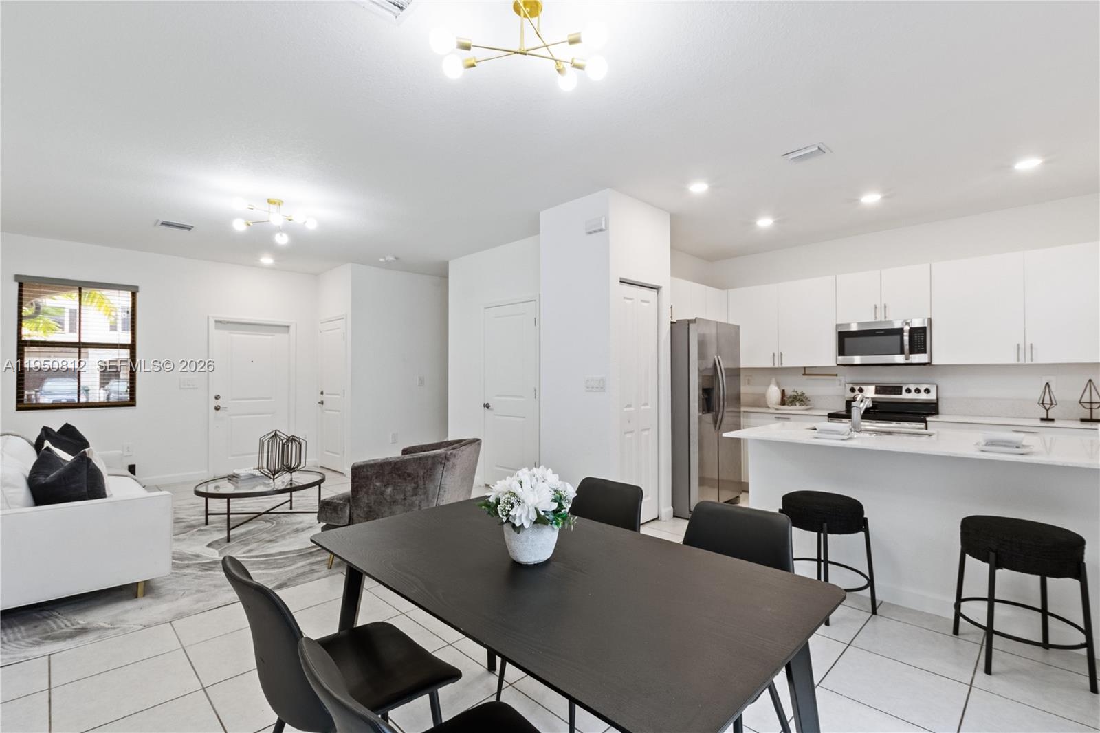 An open-concept living and dining area features white cabinetry, a kitchen island, and tiled floors — 13071 SW 232nd Ln, Miami FL 33170, MIAMI, FL