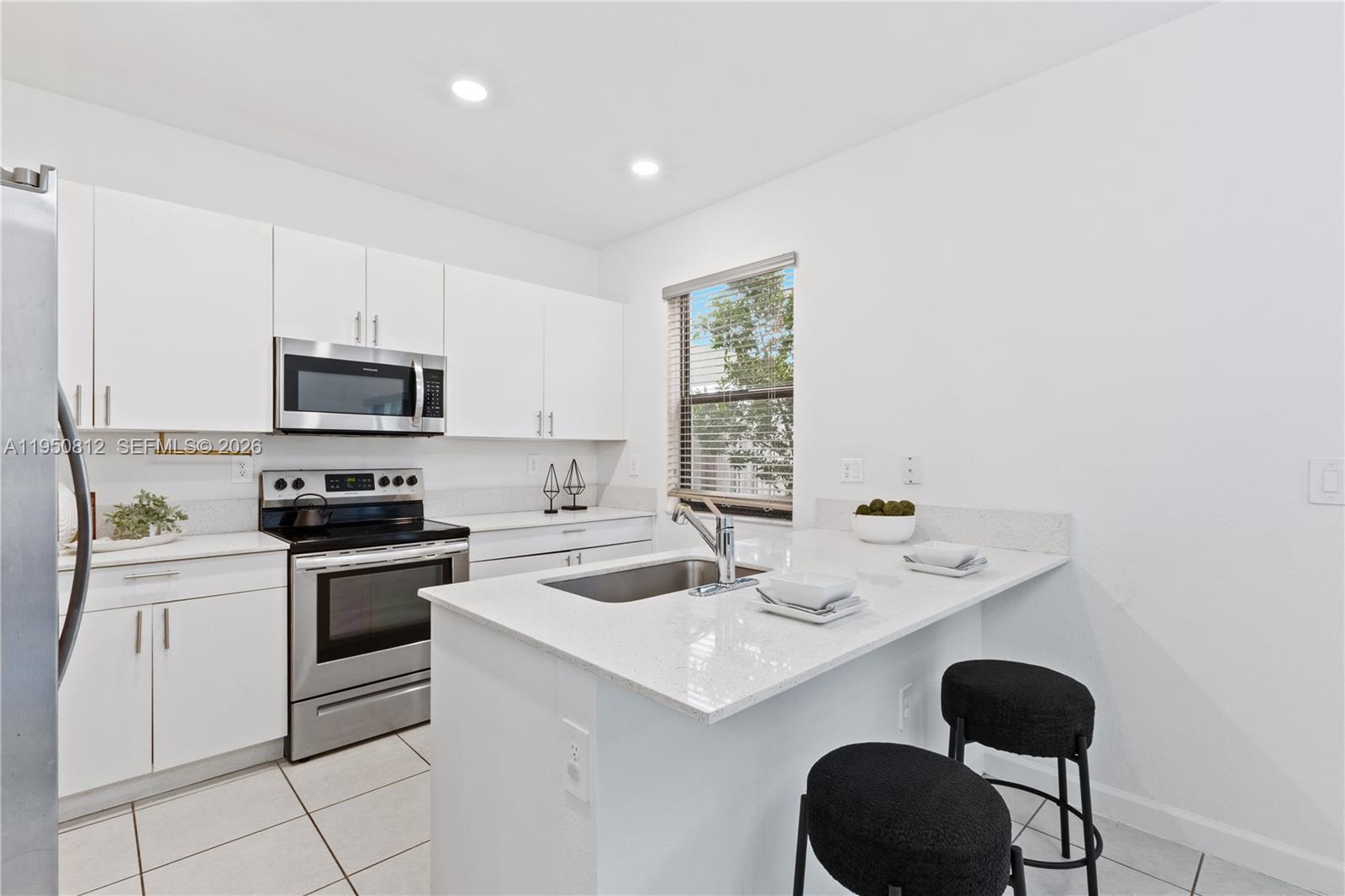 A modern kitchen features white cabinets, stainless steel appliances, and a quartz-topped breakfast bar — 13071 SW 232nd Ln, Miami FL 33170, MIAMI, FL
