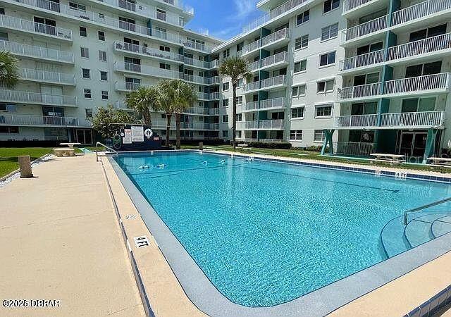 A rectangular swimming pool sits in the courtyard of a large multi-story apartment building — 2727 N ATLANTIC AVENUE UNIT 1100, DAYTONA BEACH, FL