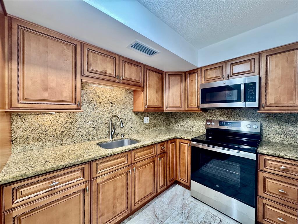 A kitchen features wood cabinets, granite countertops, stainless steel appliances, and a tile floor — 2727 N ATLANTIC AVENUE UNIT 1100, DAYTONA BEACH, FL