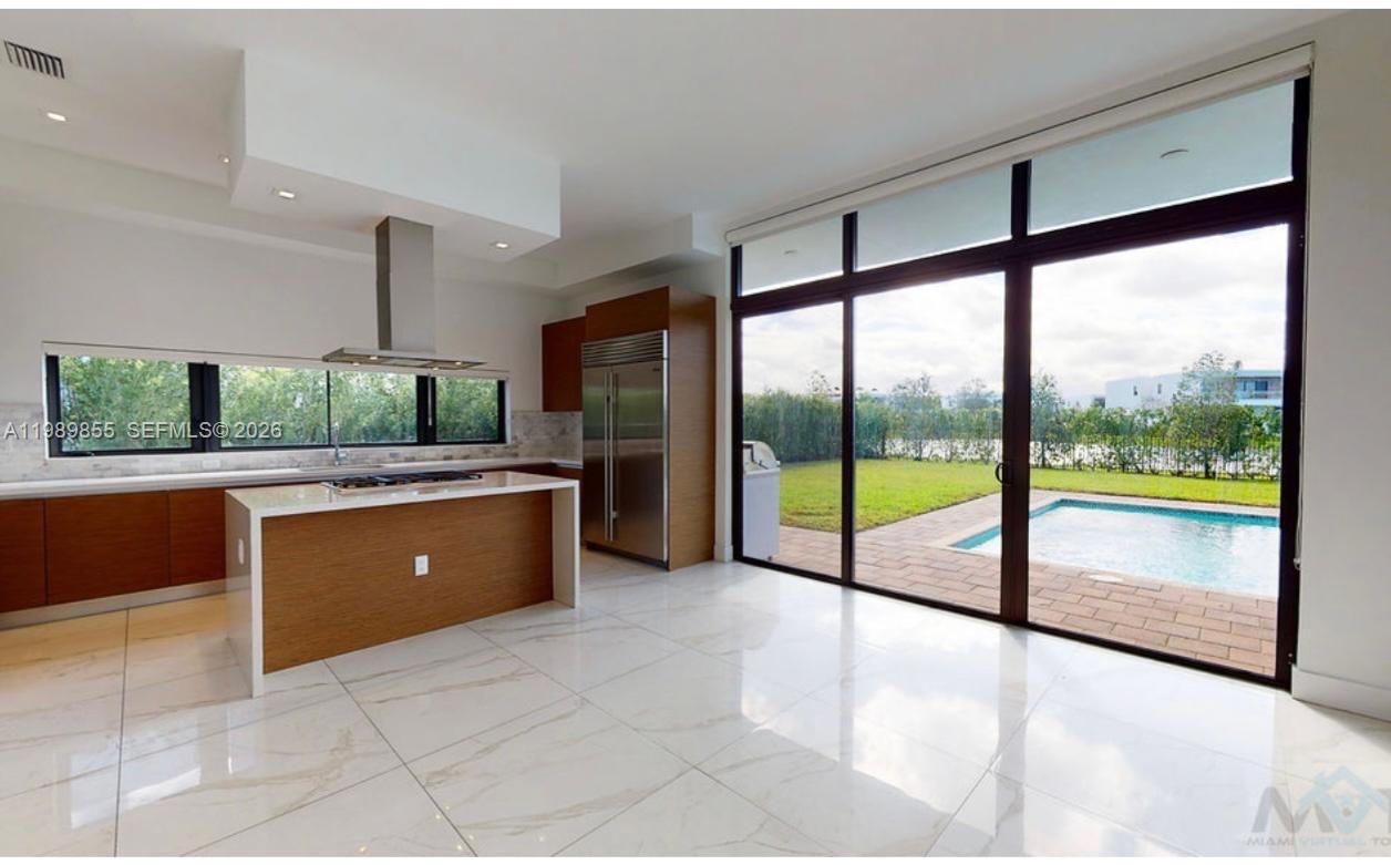 A modern kitchen with wood cabinetry and a marble island overlooks a backyard swimming pool — 16580 Sunset Way # 16580, Weston FL 33326, WESTON, FL