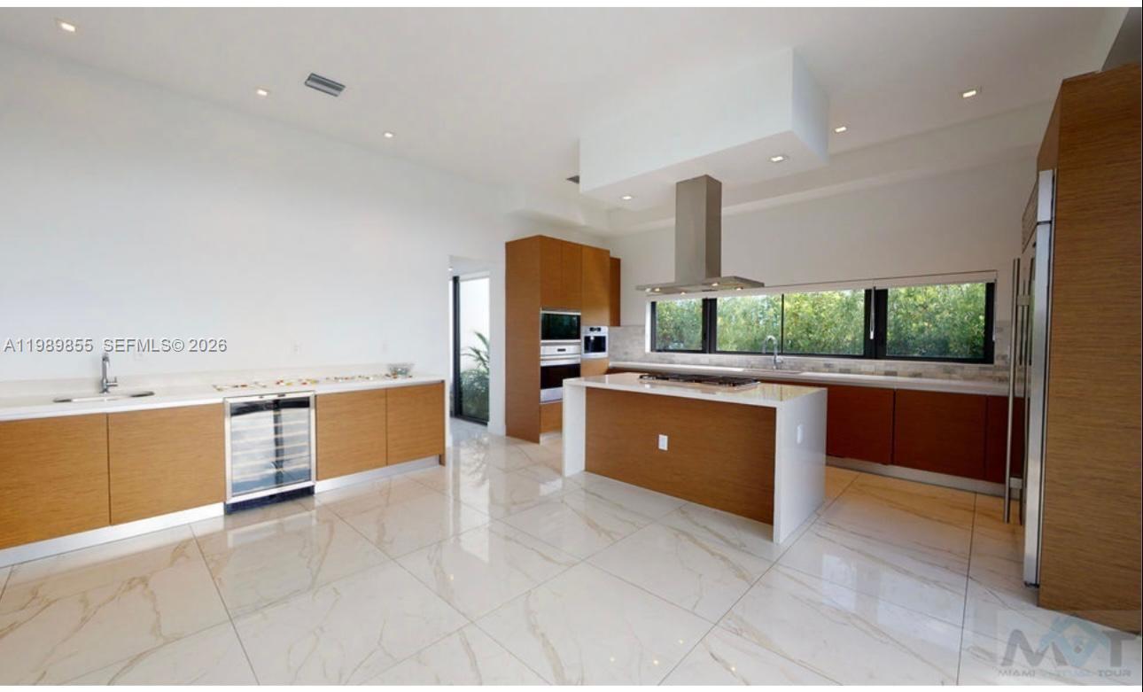 A modern kitchen features wood cabinetry, a central island with a cooktop, and marble flooring — 16580 Sunset Way # 16580, Weston FL 33326, WESTON, FL
