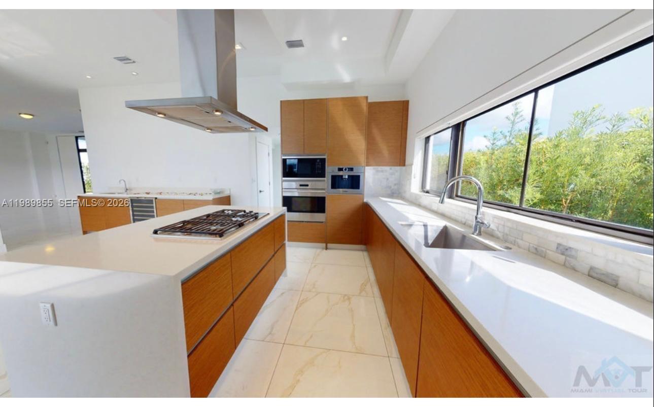 A modern kitchen features wood cabinets, white countertops, a central island, and a large window — 16580 Sunset Way # 16580, Weston FL 33326, WESTON, FL