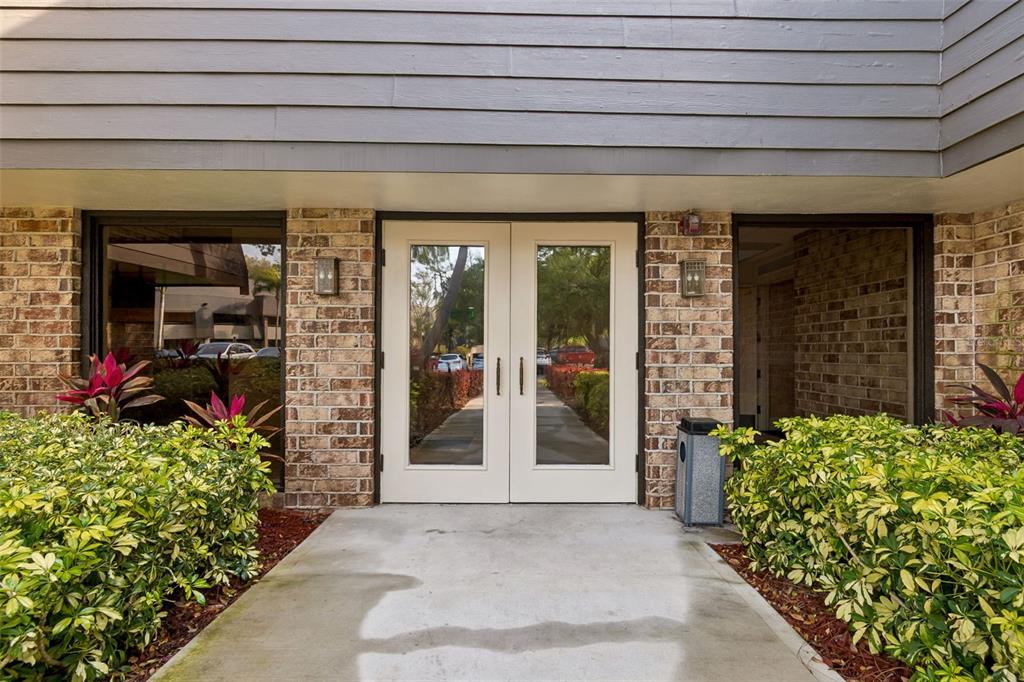 A concrete walkway leads to a set of double glass doors framed by brick walls — 36750 US HIGHWAY 19 N UNIT 8-202, PALM HARBOR, FL