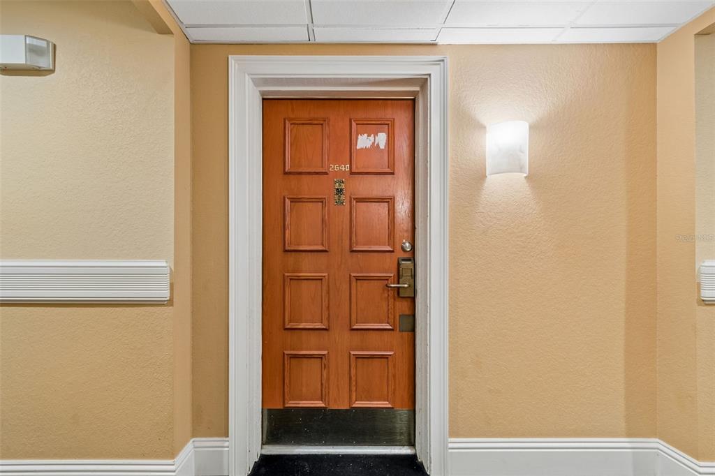 A wooden door with the number 2640 is centered in a beige hallway — 36750 US HIGHWAY 19 N UNIT 8-202, PALM HARBOR, FL