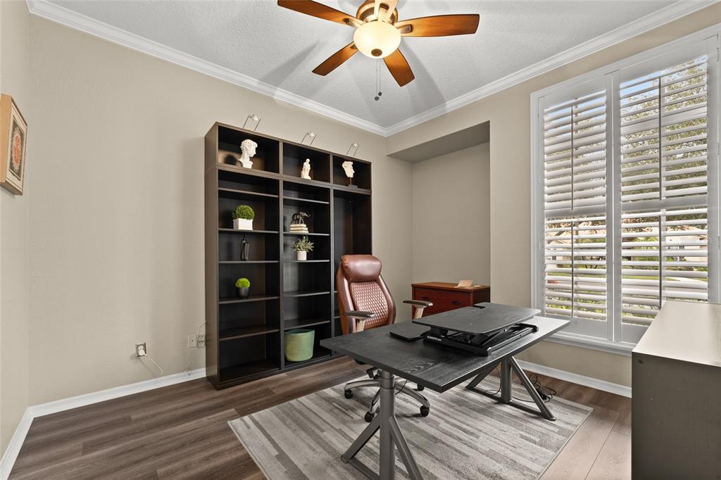 A home office features a dark wood bookshelf, a standing desk, and plantation shutters — 9502 PORTBURY DRIVE, ORLANDO, FL
