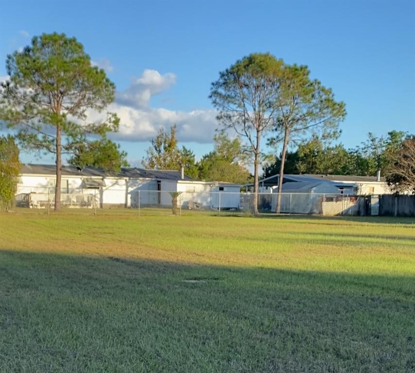 A grassy yard sits in front of two single-story houses enclosed by a chain-link fence — 0 SE SUNSET HARBOR ROAD, SUMMERFIELD, FL