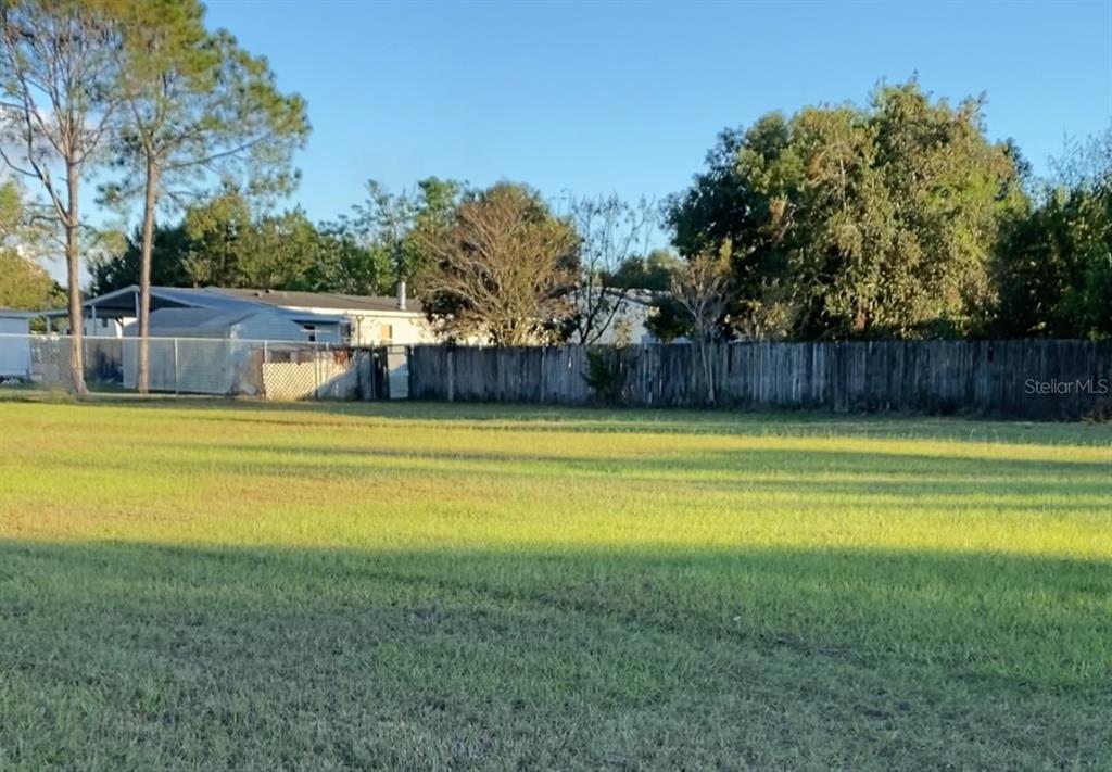 A grassy vacant lot features a wooden fence and trees in the background — 0 SE SUNSET HARBOR ROAD, SUMMERFIELD, FL