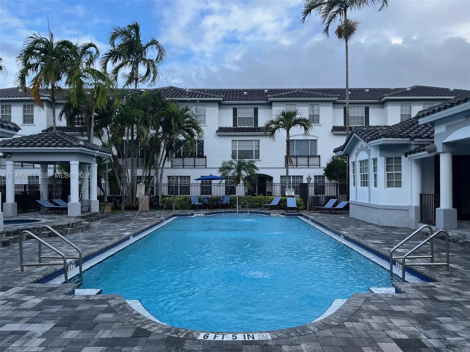 A rectangular swimming pool with a surrounding patio sits in front of a multi-story building — 781 SW 148th Ave # 1502, Sunrise FL 33325, SUNRISE, FL
