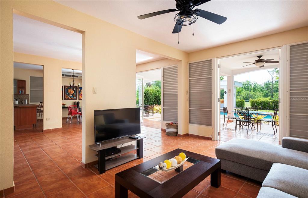A living room with tile floors, a television, and a view of an outdoor patio — 29 HACIENDA CLUB GOLF Y PLAYA, CABO ROJO, PR