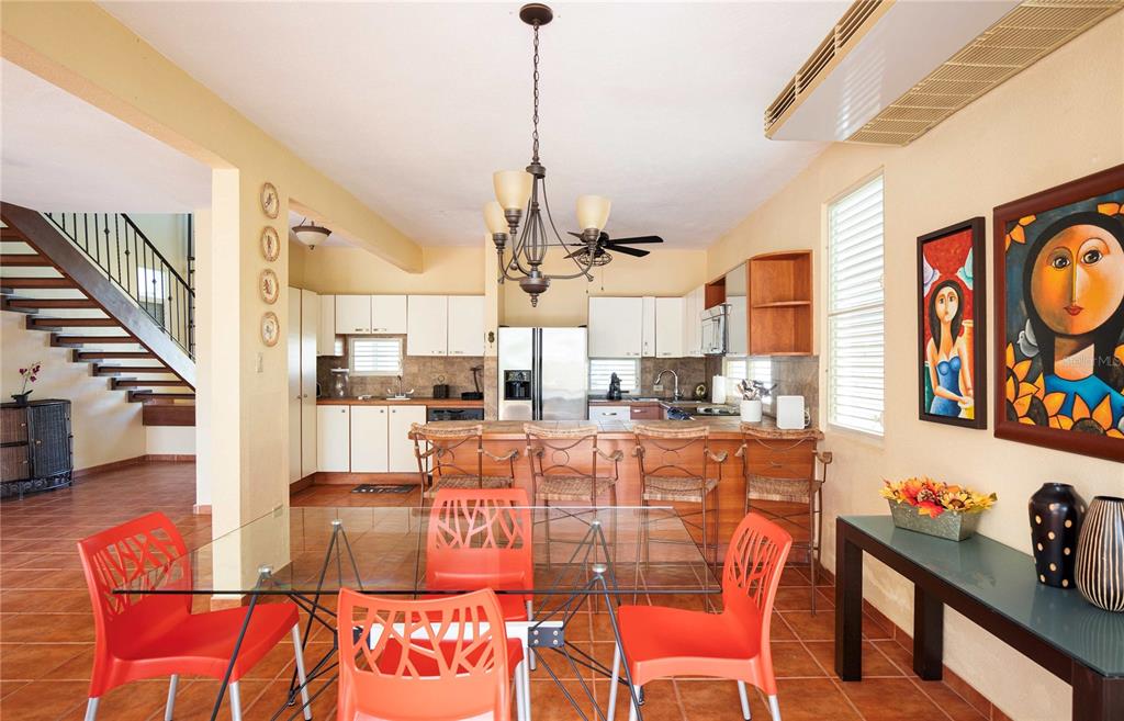 A kitchen and dining area with orange chairs, a glass table, and a wooden staircase — 29 HACIENDA CLUB GOLF Y PLAYA, CABO ROJO, PR