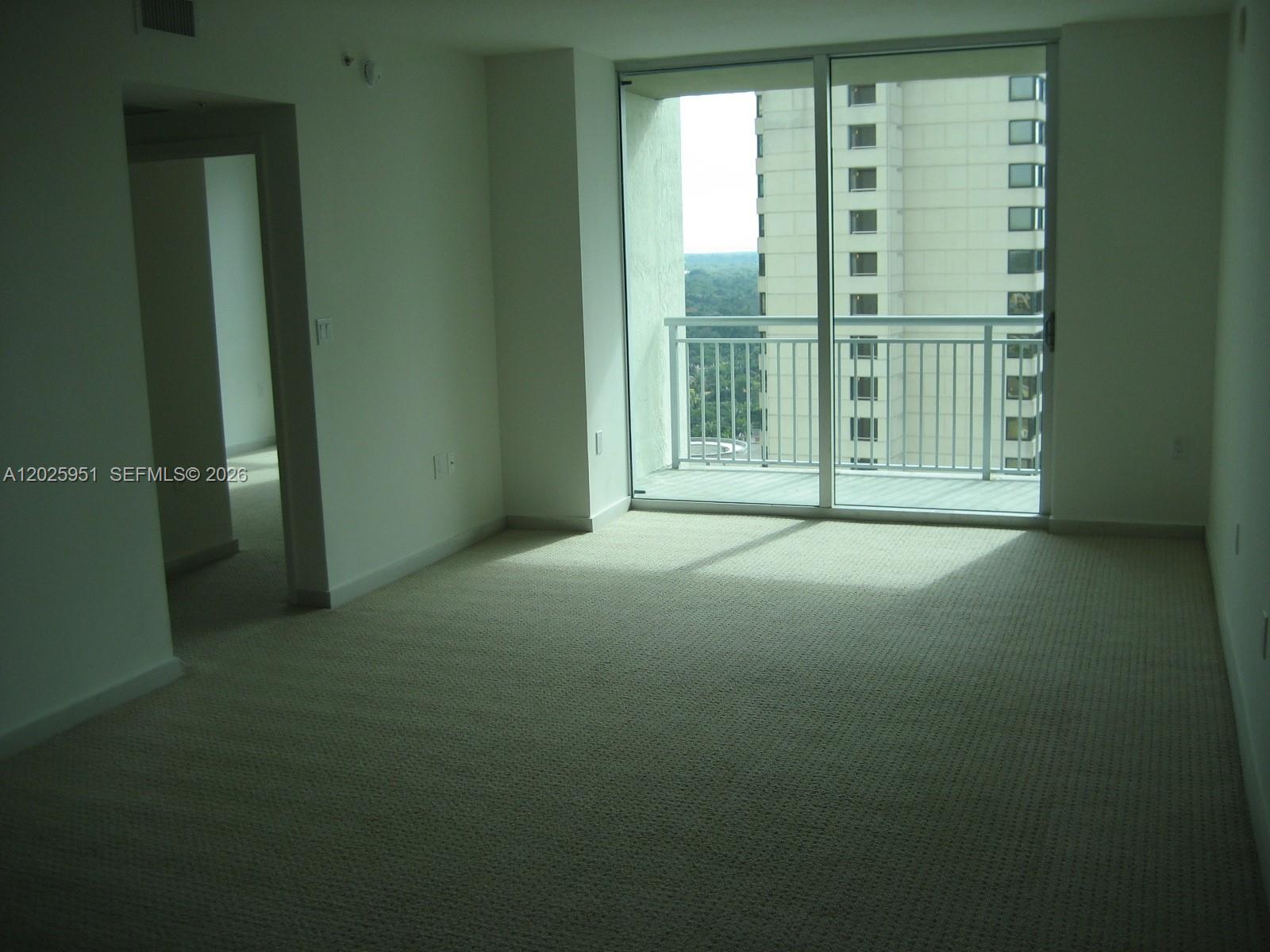 An empty room with beige carpet, white walls, and a sliding glass door to a balcony — 9066 SW 73 CT # 1802, Miami FL 33156, MIAMI, FL