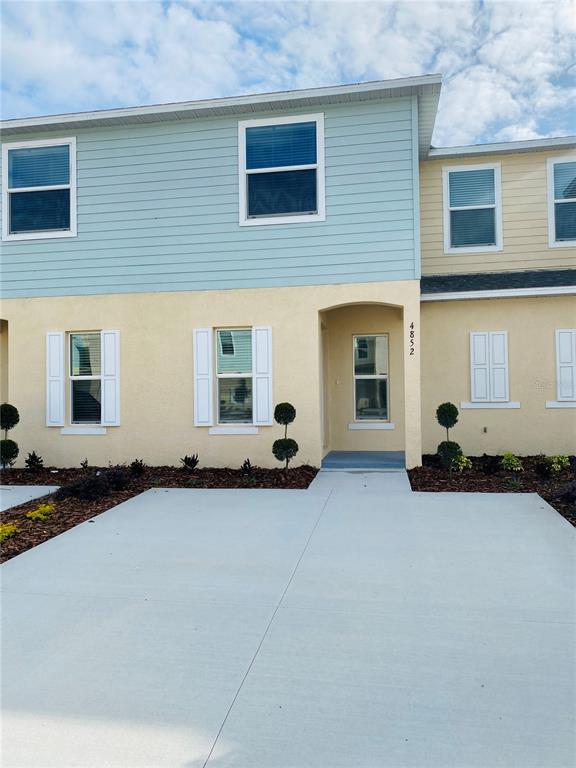 The exterior of a two-story townhouse features light blue siding, yellow stucco, and a concrete driveway — 4852 CORAL CASTLE DRIVE, KISSIMMEE, FL