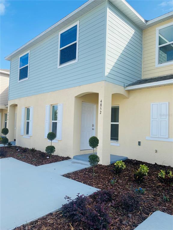 A two-story townhouse exterior features light blue siding, yellow stucco walls, and a white door — 4852 CORAL CASTLE DRIVE, KISSIMMEE, FL