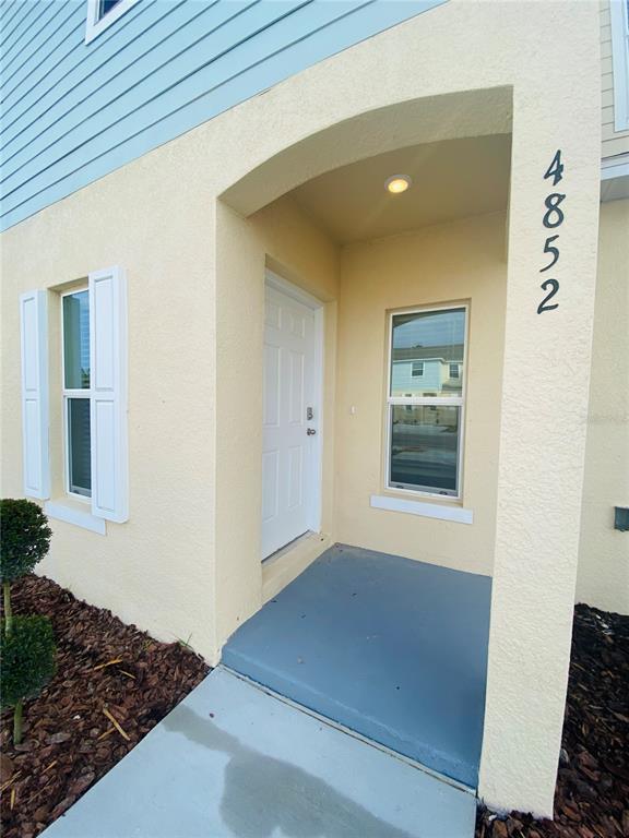 The exterior of a home features a recessed entryway with a white door and stucco walls — 4852 CORAL CASTLE DRIVE, KISSIMMEE, FL