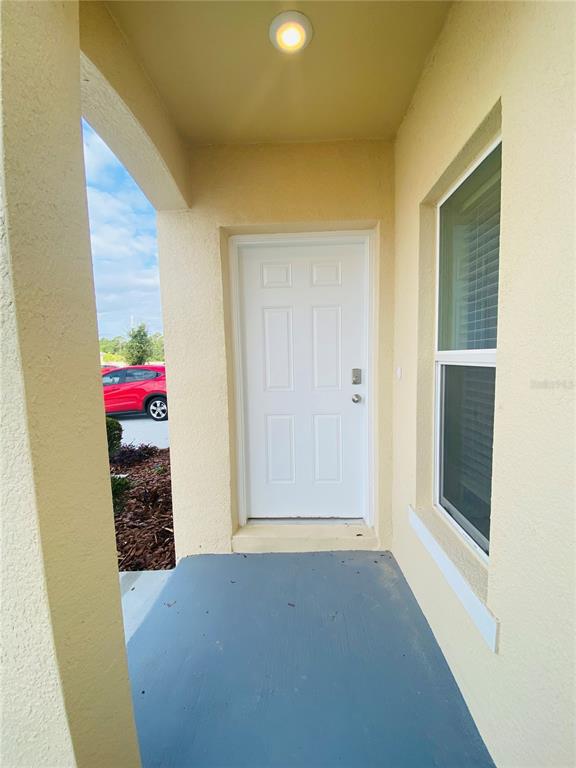 A covered entryway features a white six-panel door, a light fixture, and a gray floor — 4852 CORAL CASTLE DRIVE, KISSIMMEE, FL