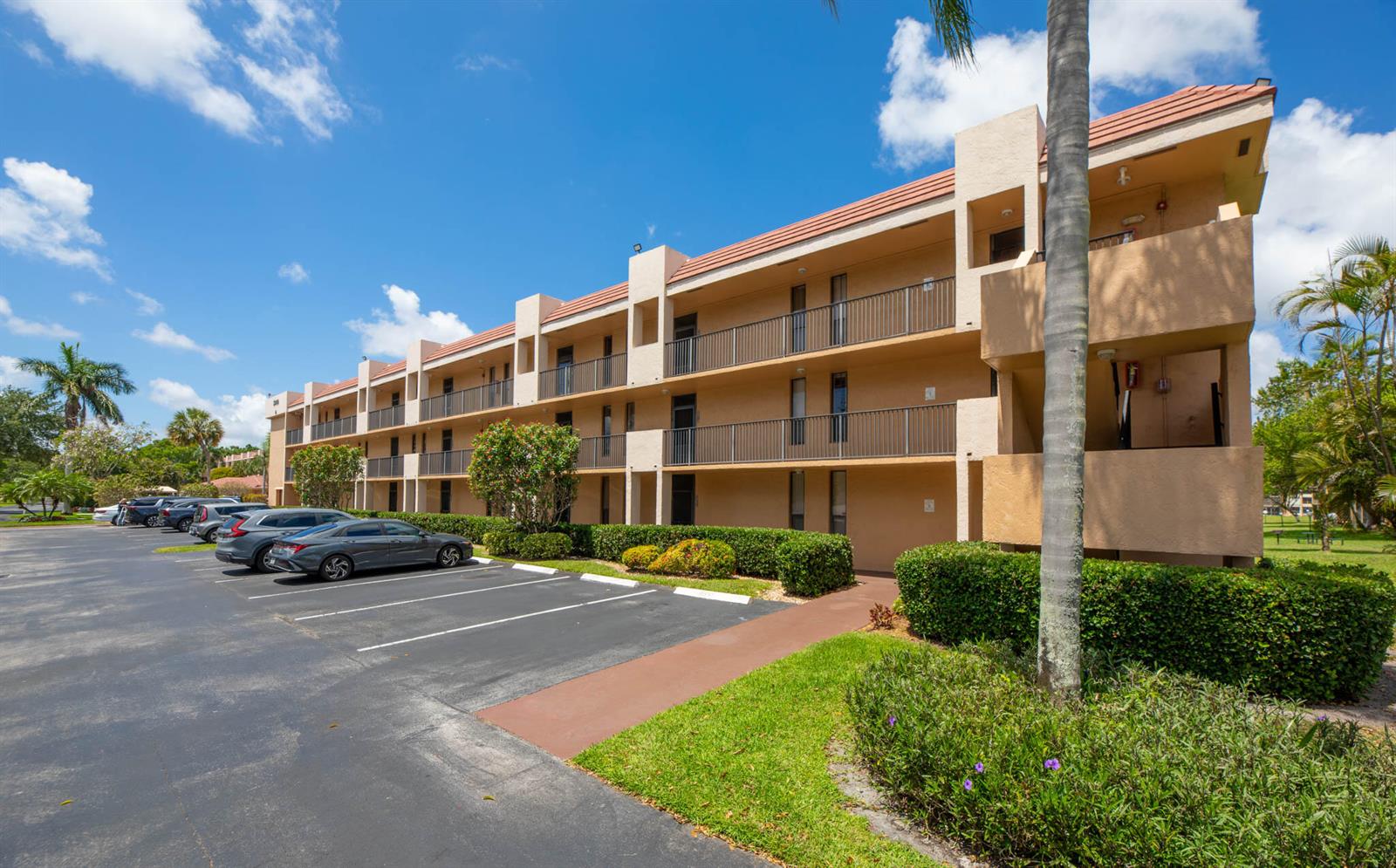 A three-story apartment building with a parking lot and landscaped grounds under a blue sky — 5926 Coral Lake Drive # 302, Margate FL 33063, MARGATE, FL