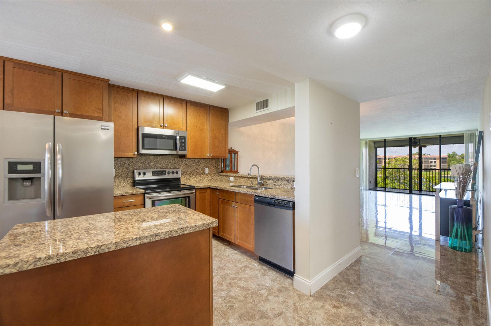 A kitchen with wood cabinets, granite countertops, and stainless steel appliances opens to a living area — 5926 Coral Lake Drive # 302, Margate FL 33063, MARGATE, FL