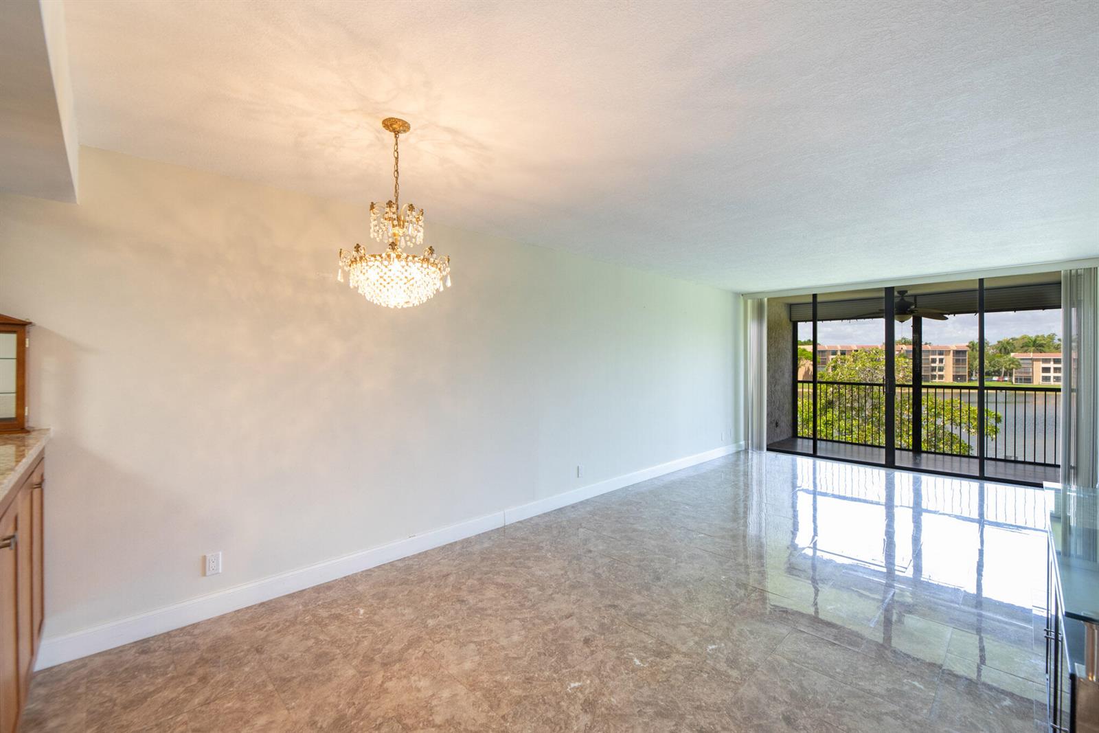 An empty dining room with a crystal chandelier, marble-look tile flooring, and a sliding glass balcony — 5926 Coral Lake Drive # 302, Margate FL 33063, MARGATE, FL