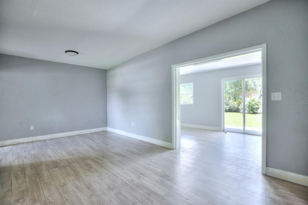 An empty room with light wood-look flooring and gray walls leads to a sunroom — 3009 MARATHON AVENUE, ORLANDO, FL