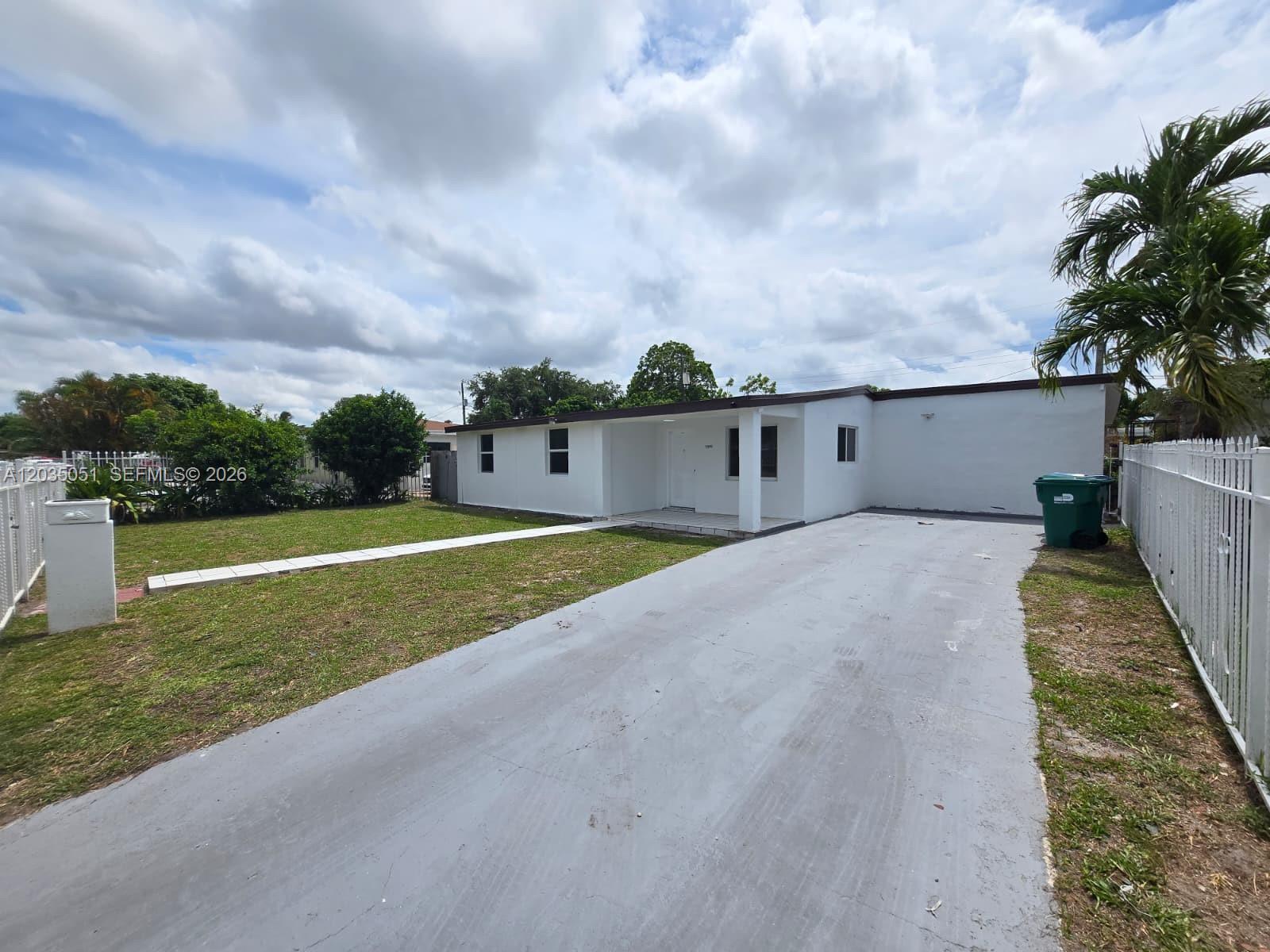 A white single-story house features a paved driveway, a front lawn, and a white fence — 9590 NW 32nd Ct, Miami FL 33147, MIAMI, FL