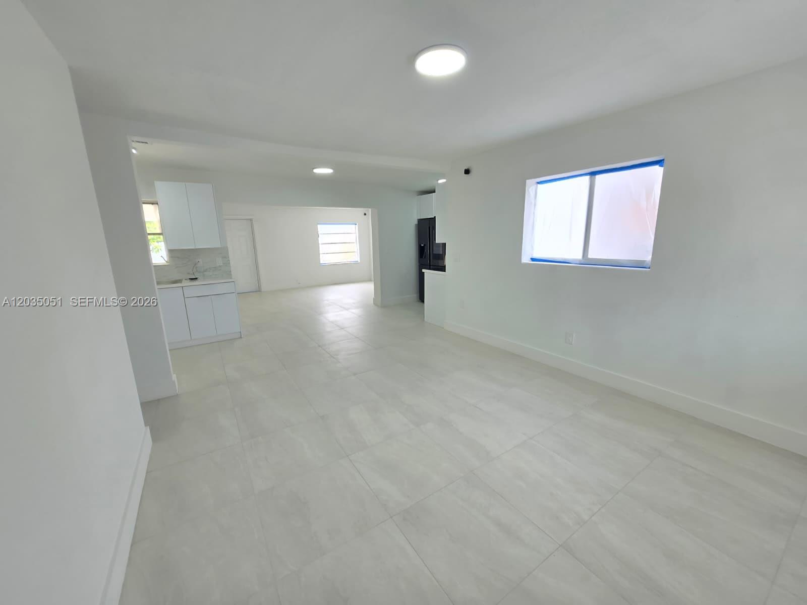 This open-concept living area features white walls, light-colored tile flooring, and a kitchen — 9590 NW 32nd Ct, Miami FL 33147, MIAMI, FL