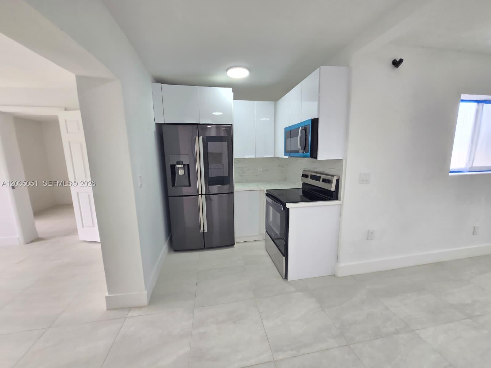 A kitchen features white cabinets, stainless steel appliances, and light-colored tile flooring — 9590 NW 32nd Ct, Miami FL 33147, MIAMI, FL