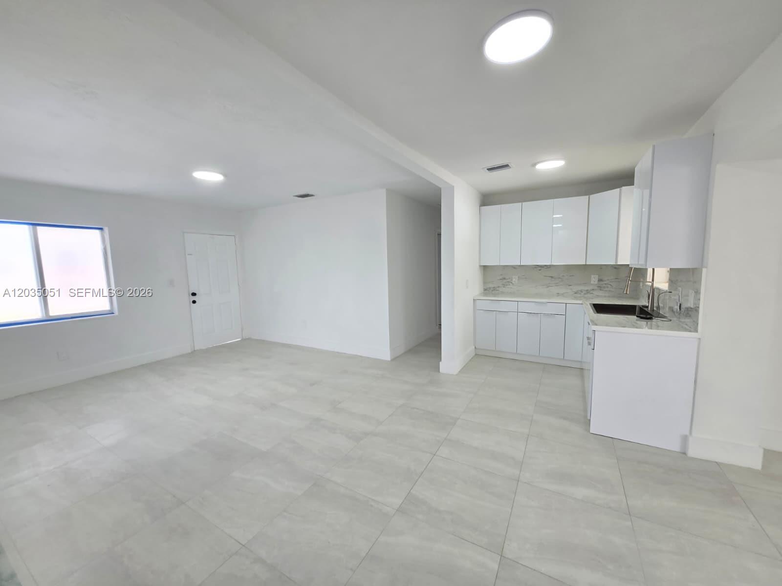 An open-concept room features white cabinets, marble-look countertops, and light-colored tile flooring — 9590 NW 32nd Ct, Miami FL 33147, MIAMI, FL