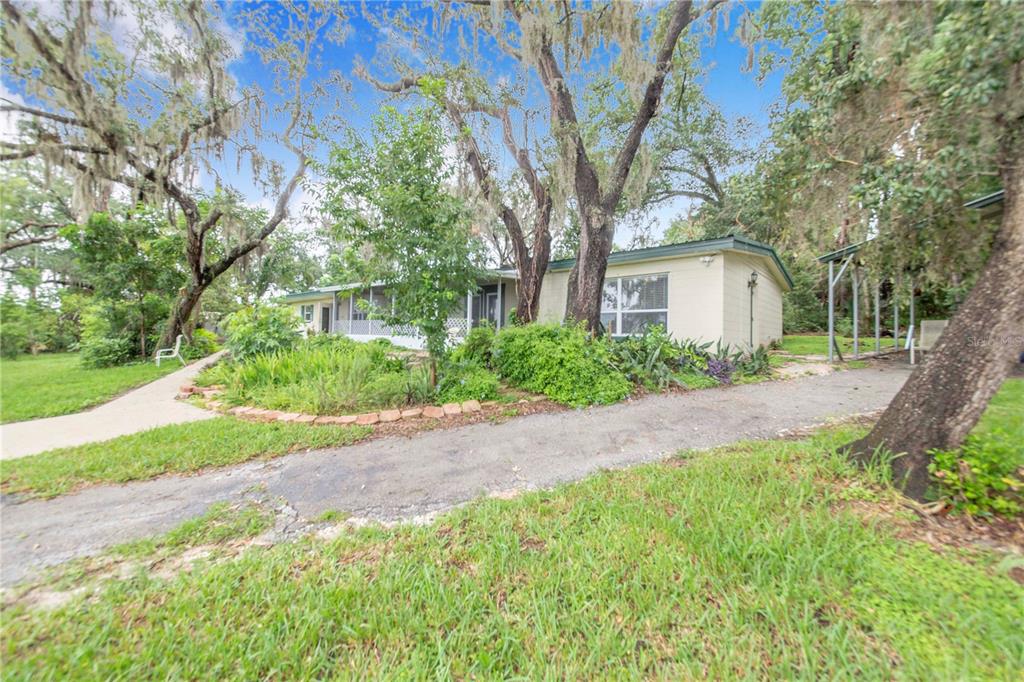 A single-story house with a light-colored exterior, a screened porch, and mature trees in front — 490 TWIN LAKES BOULEVARD, LAKE ALFRED, FL