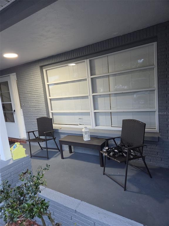 A covered porch features gray brick walls, two dark chairs, and a small matching table — 5344 NANCY LANE, HOLIDAY, FL