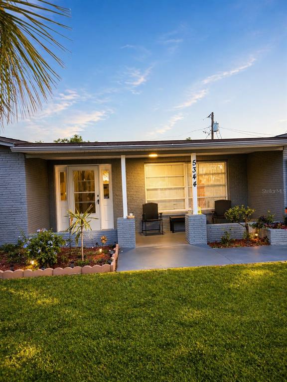A gray brick house features a covered front porch with two chairs and a lawn — 5344 NANCY LANE, HOLIDAY, FL