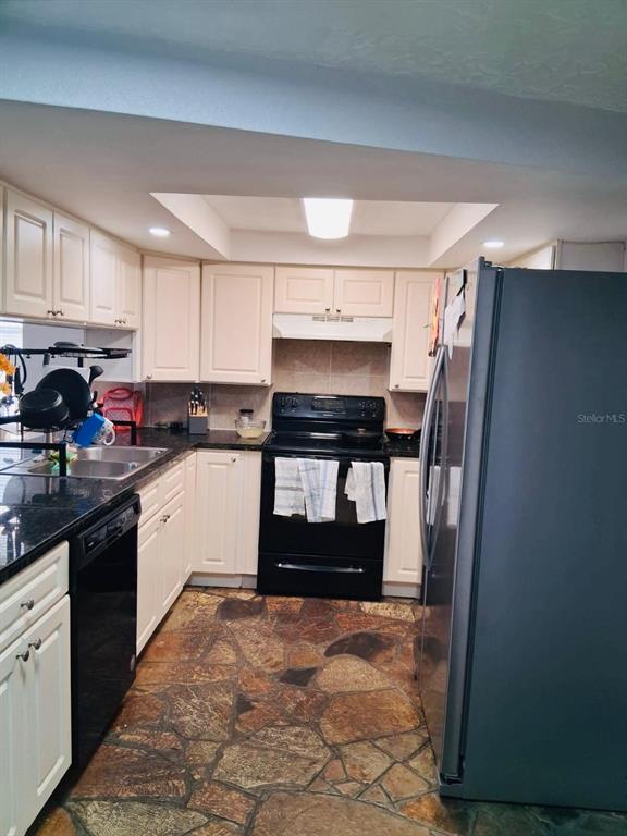 A kitchen features cream cabinets, black appliances, dark countertops, and a flagstone floor — 5344 NANCY LANE, HOLIDAY, FL