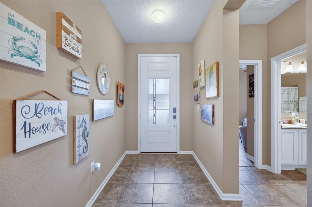 A tiled entryway features a white front door and walls decorated with beach-themed artwork — 344 TUSCANY CHASE DRIVE, DAYTONA BEACH, FL