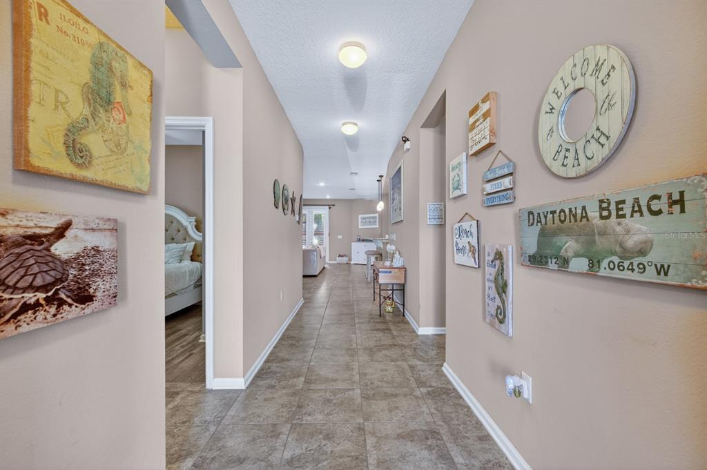 A tiled hallway leads past a bedroom and wall decor toward a bright living area — 344 TUSCANY CHASE DRIVE, DAYTONA BEACH, FL