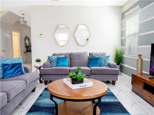 A living room features a grey sofa, a round wooden coffee table, and two wall mirrors — 1568 MAIDSTONE COURT, DAVENPORT, FL