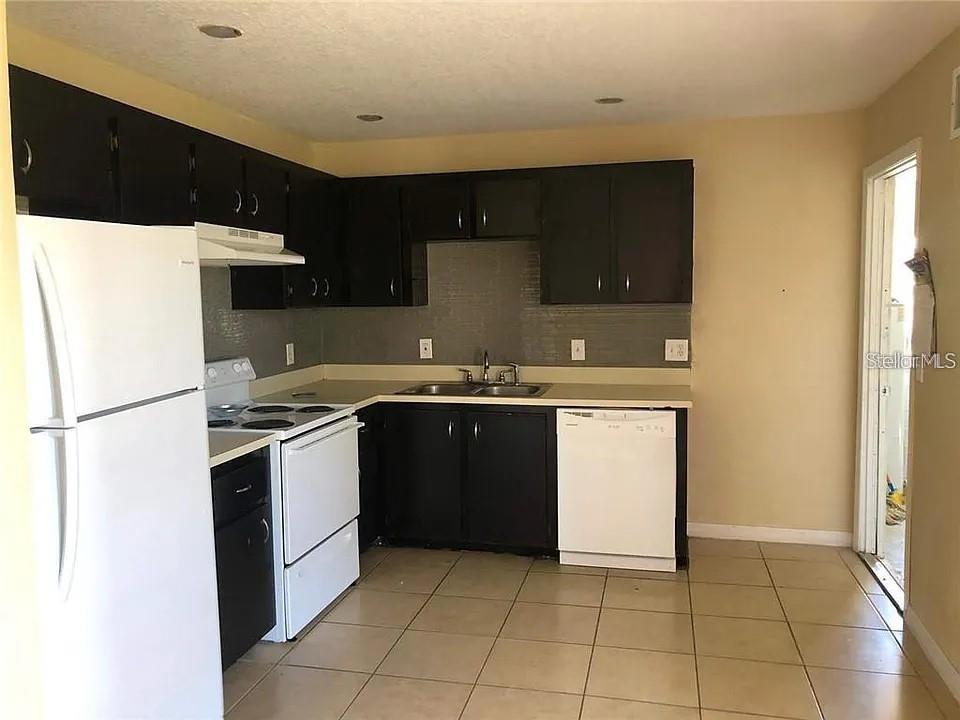 A kitchen features black cabinets, white appliances, a double sink, and light-colored tile flooring — 330 COLONADE COURT, KISSIMMEE, FL