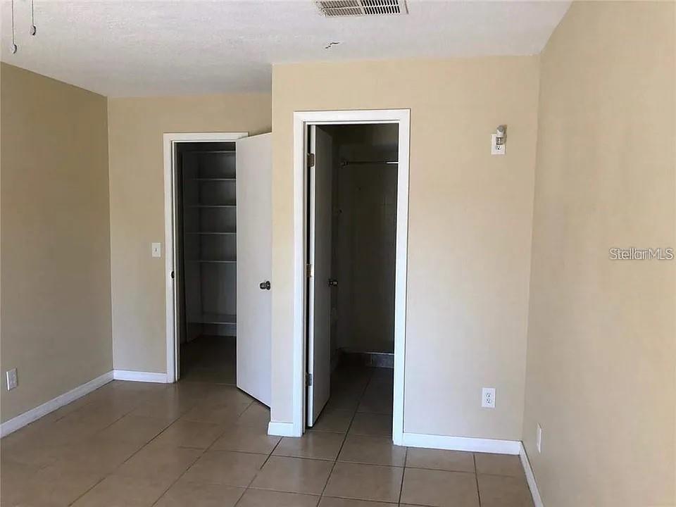 A room with tan walls, tile flooring, and two open doorways leading to a closet and bathroom — 330 COLONADE COURT, KISSIMMEE, FL