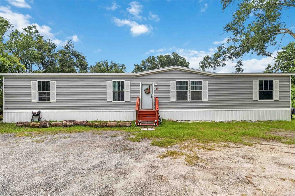 A single-story manufactured home with grey siding and a red wooden front porch — 4235 PINE TREE DRIVE, ST CLOUD, FL