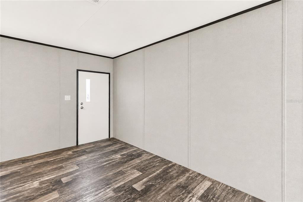 An empty room features light gray walls, dark wood-look flooring, and a white entry door — 4235 PINE TREE DRIVE, ST CLOUD, FL