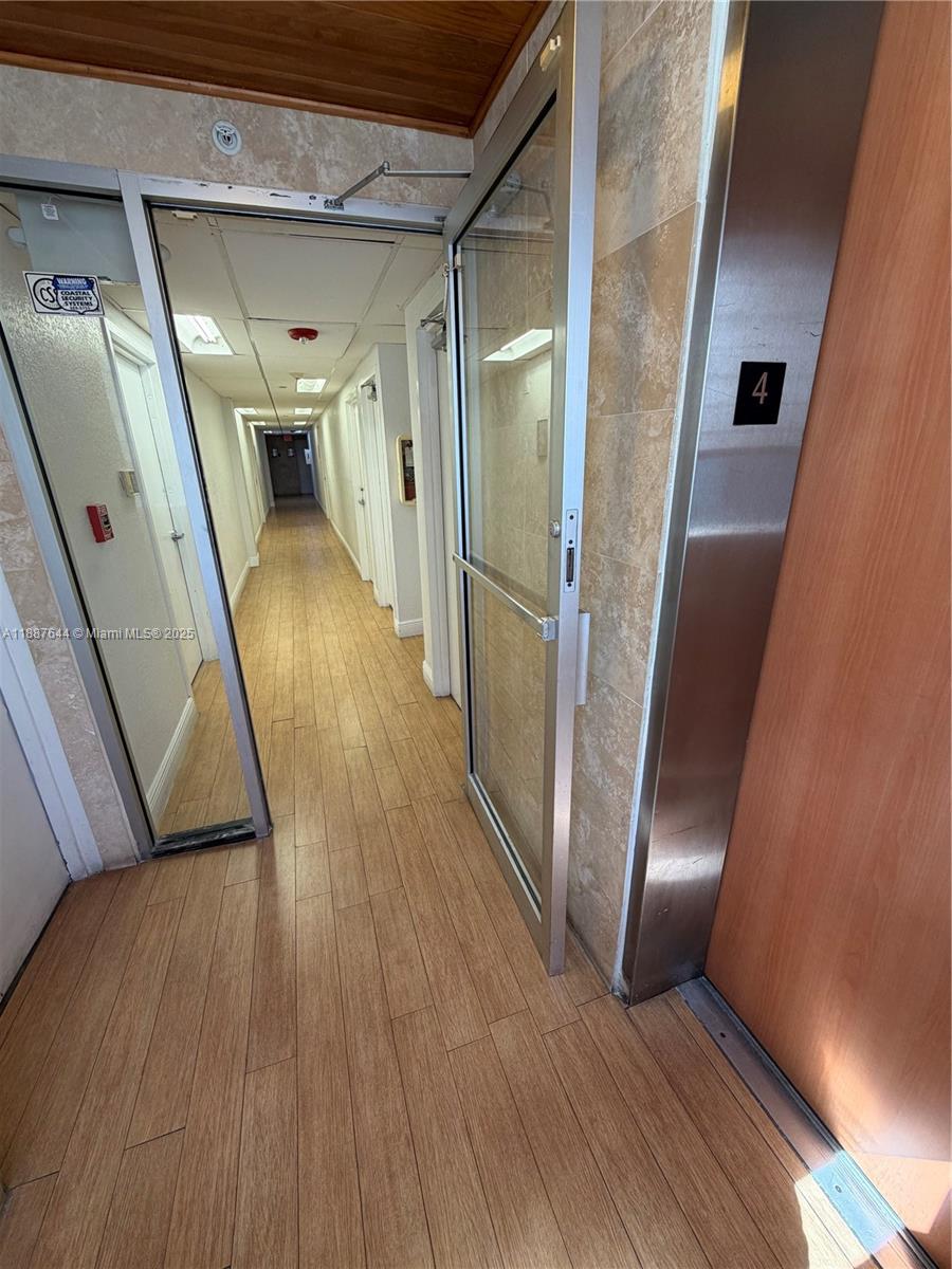 A hallway with wood-look flooring leads from an elevator lobby through a glass door — 4011 W Flagler St # 404, Miami FL 33134, MIAMI, FL