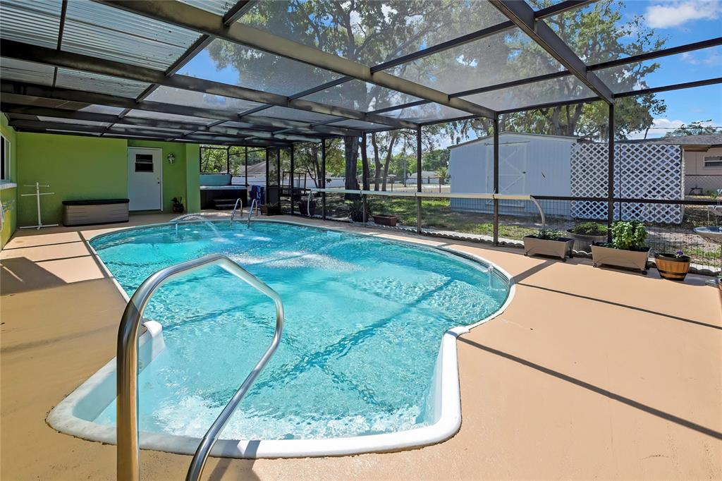 A screened-in swimming pool with a tan deck and a white shed in the background — 6100 PIEDMONT DRIVE, SPRING HILL, FL