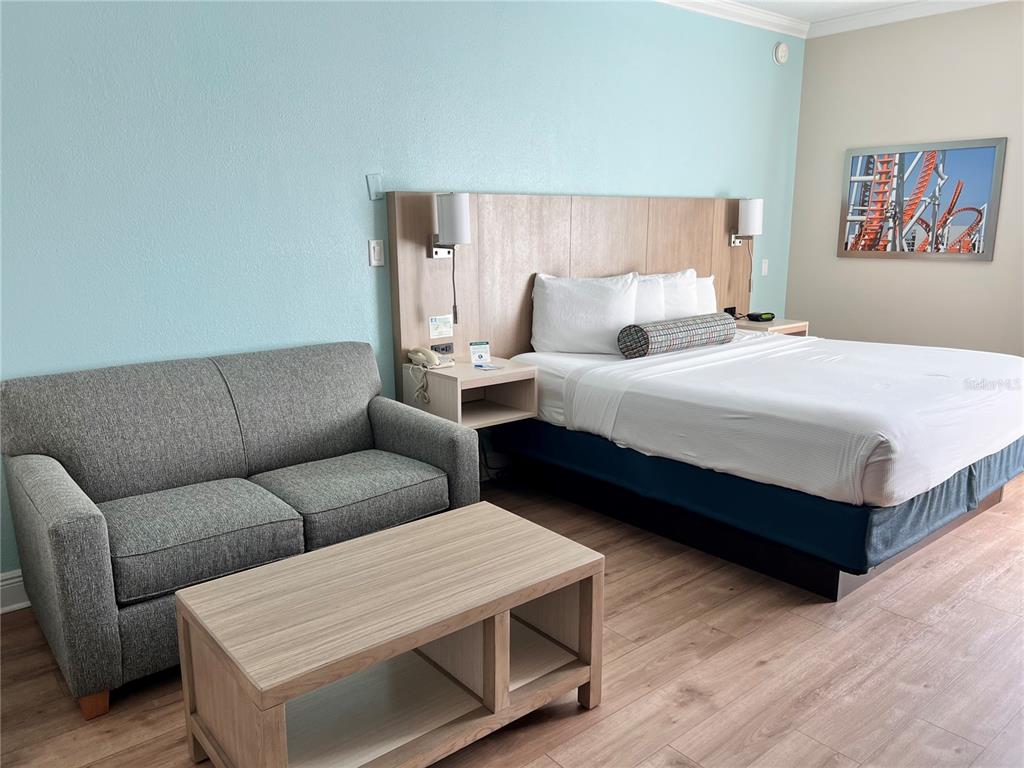 A hotel room features a gray sofa, a wooden coffee table, and a queen bed — 3000 MAINGATE LANE UNIT 506, KISSIMMEE, FL