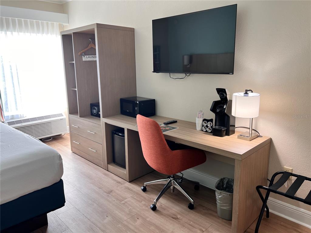 A hotel room features a desk, an orange chair, a television, and a wardrobe unit — 3000 MAINGATE LANE UNIT 506, KISSIMMEE, FL