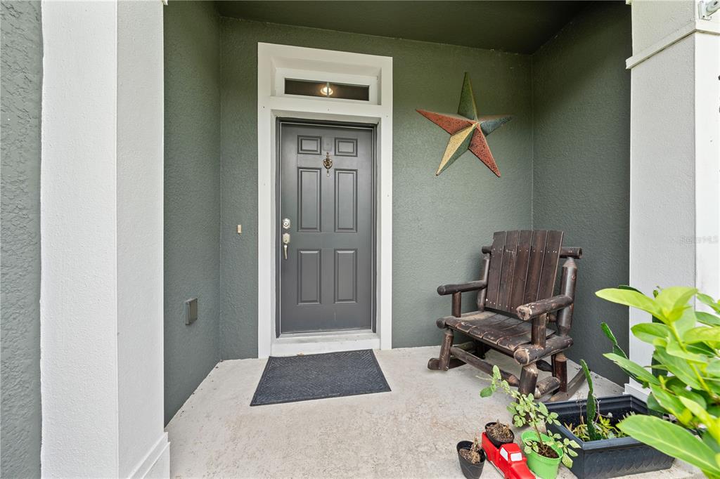 A covered front porch features a dark gray door, a wooden rocking chair, and decor — 4811 NATHAN HALE BOULEVARD, ST CLOUD, FL