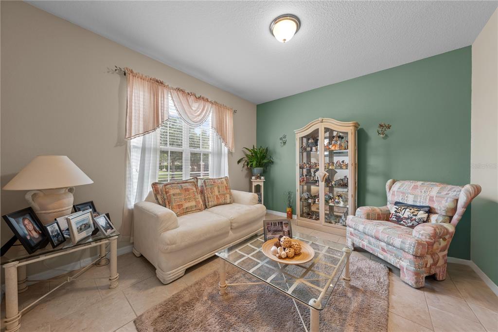 A living room features a beige sofa, patterned armchair, glass coffee table, and display cabinet — 4811 NATHAN HALE BOULEVARD, ST CLOUD, FL