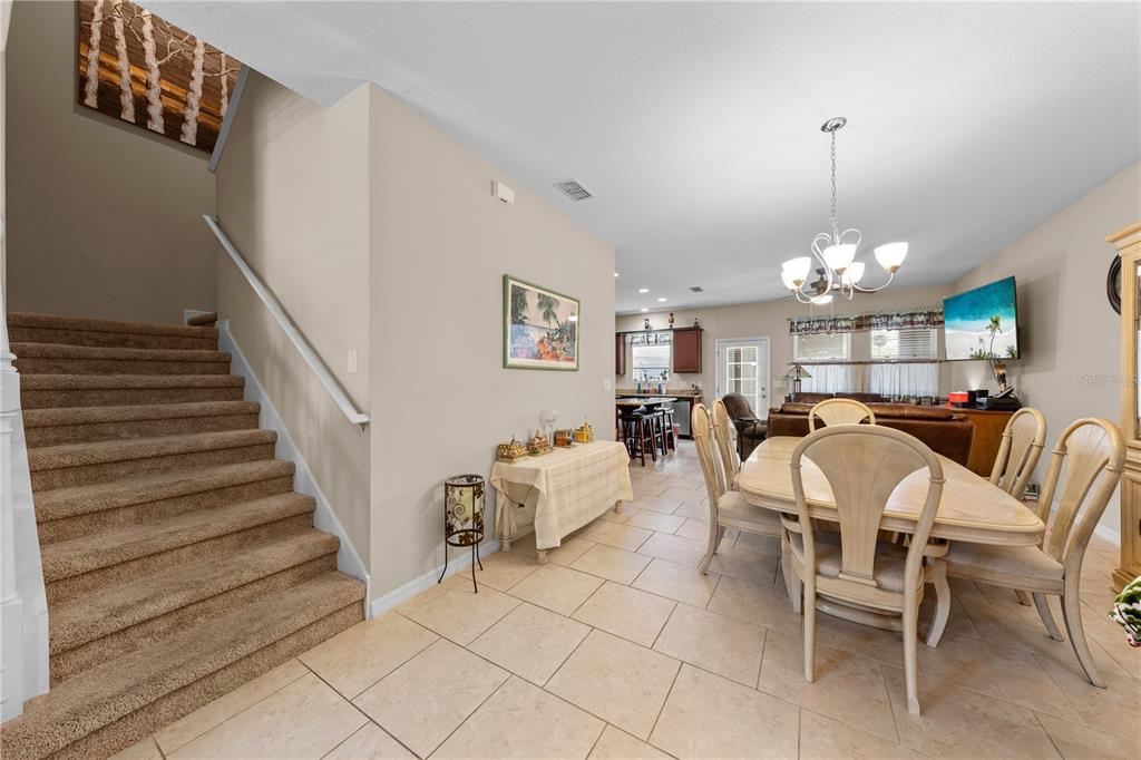 A carpeted staircase leads upstairs next to a dining area with tile flooring and furniture — 4811 NATHAN HALE BOULEVARD, ST CLOUD, FL