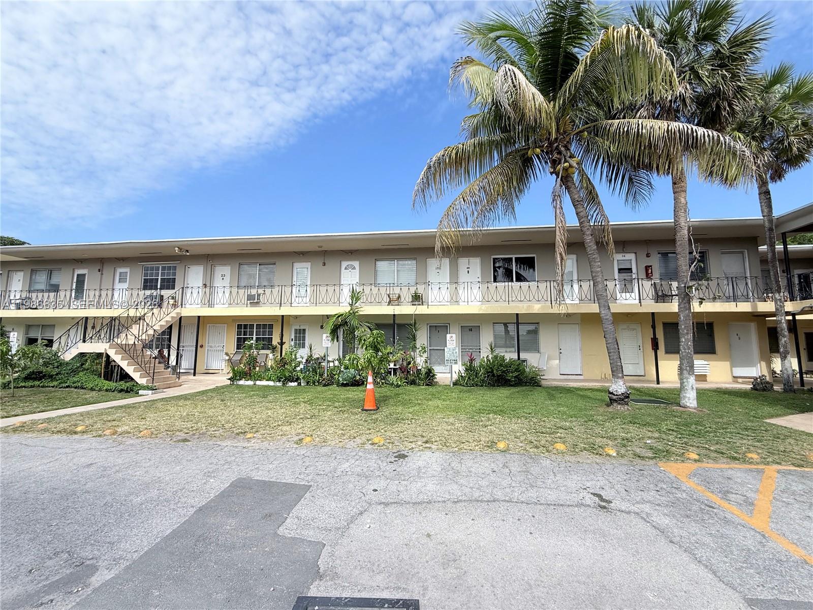 A two-story apartment building features a balcony, exterior staircases, and palm trees on a lawn — 70 NW 77th St # 9, Miami FL 33150, MIAMI, FL