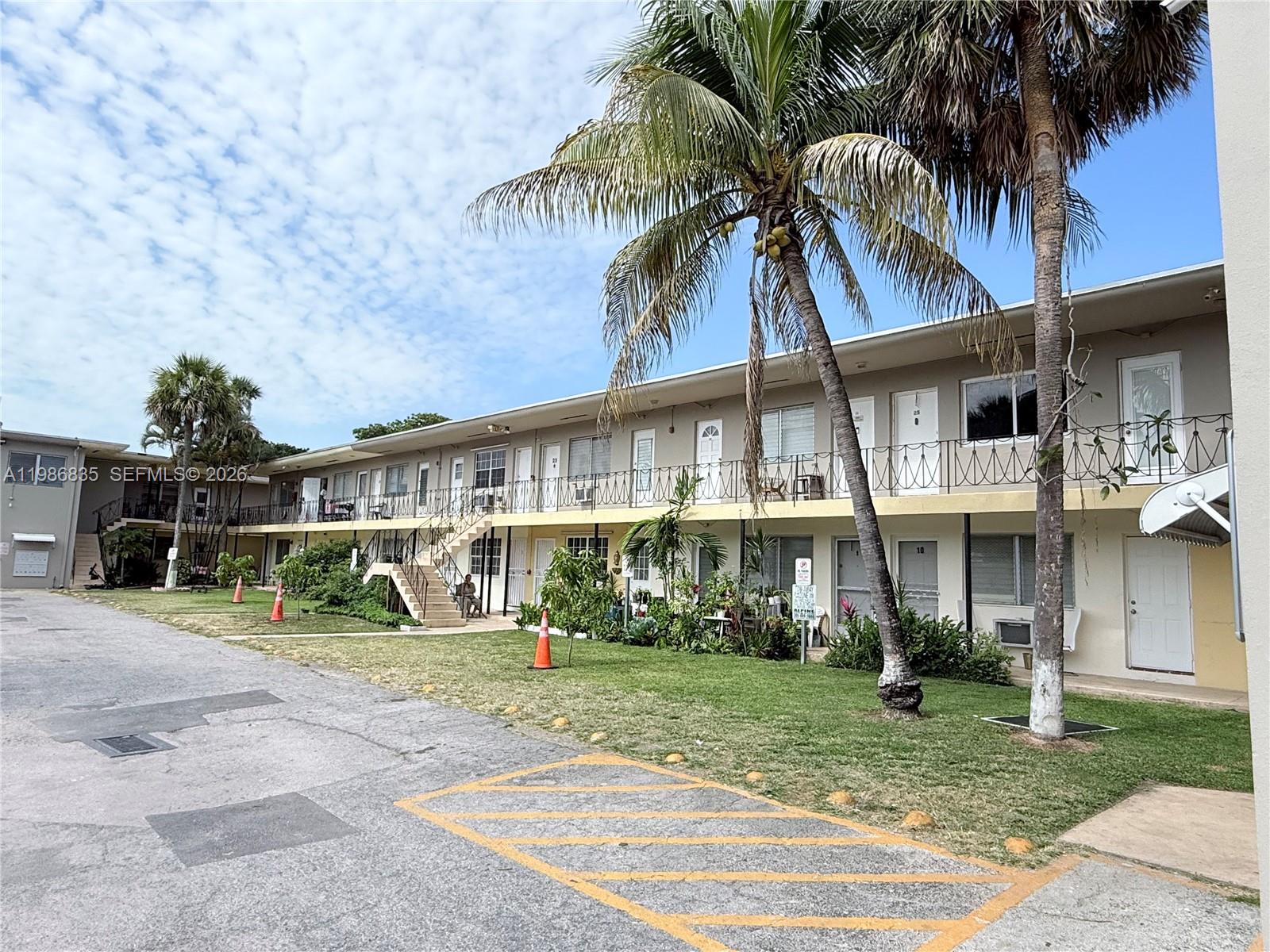 A two-story apartment building features exterior walkways, metal railings, and palm trees in front — 70 NW 77th St # 9, Miami FL 33150, MIAMI, FL