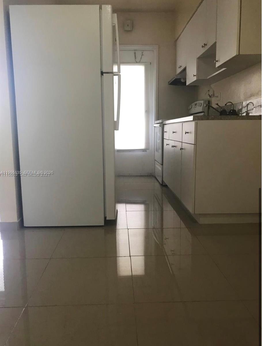 A kitchen features white cabinets, a white refrigerator, and light-colored tile flooring — 70 NW 77th St # 9, Miami FL 33150, MIAMI, FL
